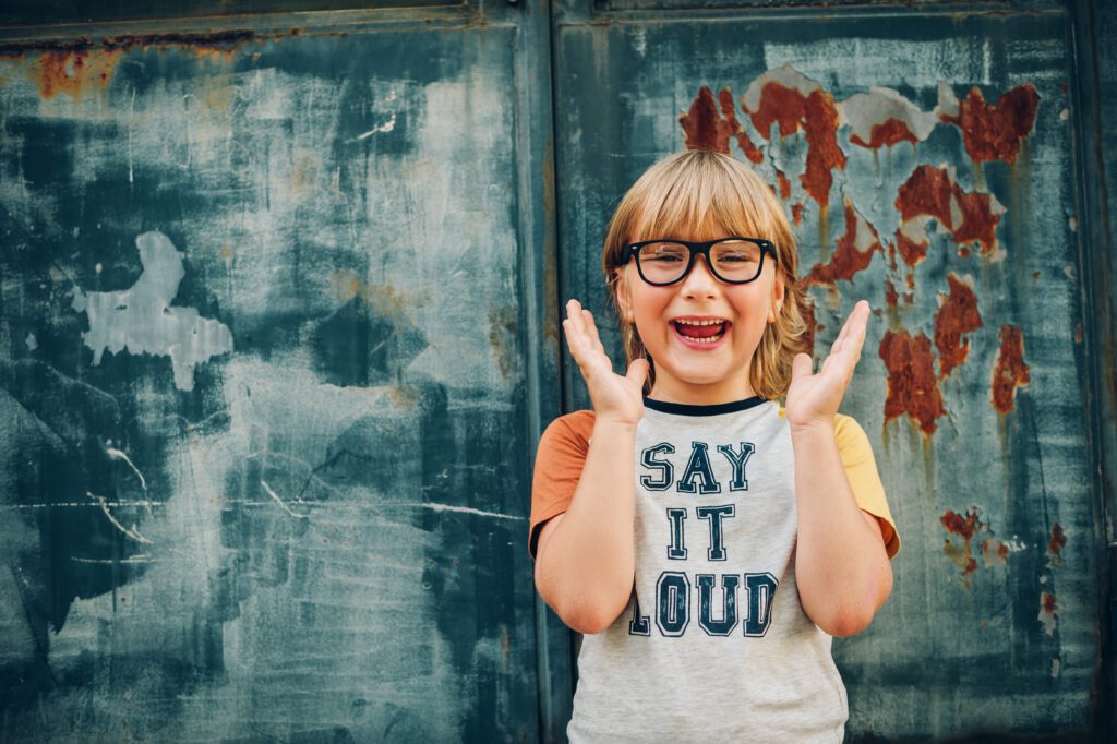 Outdoor portrait of kid wearing glasses and t-shirt that reads "Say It Loud"